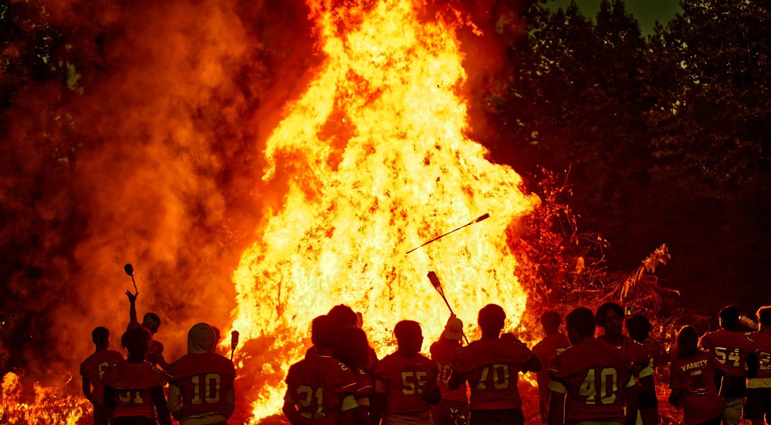 Mineola football players toss tiki torches onto the inferno.